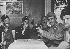 a black and white photograph of uniformed males seated around a table, several are holding glasses