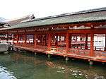 A wooden roofed corridor on stilts over water with red beams and red handrails.