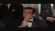 Video clip from the film, set in a casino. A woman at the table, wearing a red dress, asks "Mister..." and a man in a suit answers "Bond, James Bond" as he lights his cigarette.