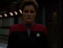 Kate Mulgrew in costume as Captain Janeway looks away from Neelix and Tuvok as she walks out of the sickbay towards the camera—the door opening and closing for her automatically—before pausing momentarily in the corridor as she walks out of frame.