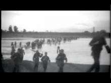 Video of American soldiers and Filipino guerrillas walking in a line through water carrying guns.