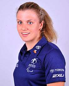 A blonde haired woman wearing her hair in a ponytail, and wearing a blue polo shirt