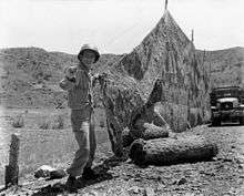 A man in military uniform constructs a net in a hilly outdoor environment