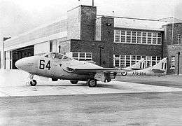 Side view of single-engined, twin-boomed military jet parked in front of a building