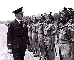 Man in dark military uniform with peaked cap inspecting troops at a parade