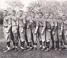 Ten baseball players, standing in size order with the tallest on the left. They are wearing baseball uniforms without their caps.