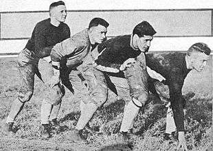 Four football players in uniform prepared to run, standing one behind the other