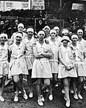 black and white photo of a group of women wearing light coloured dresses, with hair bands in their hair
