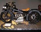 A shiny black Art Deco motorcycle of 1923 with a BMW logo on the gas tank and a boxer twin engine.