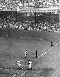 A black and white image of right field and first base in a baseball diamond in a large stadium with filled stands. A runner is rounding first.