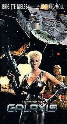 Brigitte Nielsen, holding a futuristic gun, stands in front of a spaceship