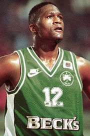 Dominique Wilkins is taking a rest during a 1996 Panathinaikos Euroleague game. His #12 uniform is green with the Beck's beer logo on the front.
