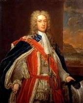 A three-quarter portrait of a man wearing 18th-century dress.  He wears a white frock, under a red coat, topped by a blue gown.  He wears a large gold chain around his neck, which descends as far as his chest.  He has a long white wig, and behind him a portrait of a shoreline is visible.