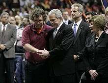 President Bush clasping one of the hands of a student in both of his; President Bush's wife, Laura, is to his left.