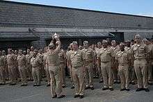 A sailor holds up a trophy in front of a formation of sailors