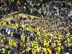 Fans wearing maize swarm the basketball court in celebration.