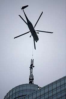 A close up view of a helicopter transporting the steeple of a building either to or from the top of the building