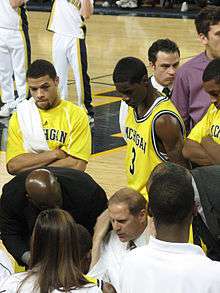 Basketball players in maize uniforms look on as coach gives instructions in the huddle.