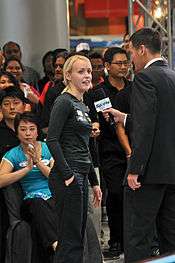 Woman stands by microphone held by a man dressed in a suit