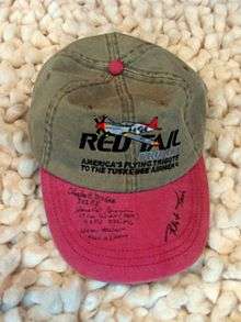 a gray baseball cap with light red brim. The cap has a Red Tail Project logo and the brim has several autographs.