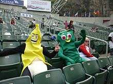 Two people dressed in fancy costume (Gumby - right; Banana – left) seated in stadium