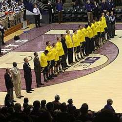 Michigan basketball team in blue uniforms with gold (maize) tops during the national anthem