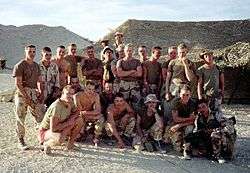A group of Marines in desert camouflage posing outside their rest areas.