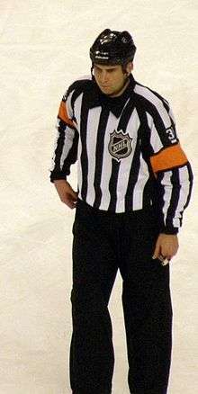A man wearing a striped shirt with orange armbands, on the ice during a hockey game