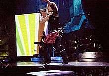 Madonna wearing a skirt dancing on a blue it stage, in front of a video screen.