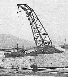 A large crane being towed by a boat in the water