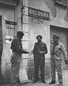 Three standing officers looking at a map under a sign reading Bologna