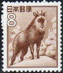 A postage stamp featuring a sepia illustration of a goat-antelope standing on a snow-covered, forested hilltop.  Stylized Japanese writing in the top left corner reads: "日本郵便".  Immediately below this writing is a large "8".