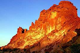 Rainbow Valley's main sandstone formation, a steep and wide bluff, glowing red, orange and yellow in the light of the setting sun