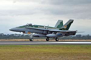 Side view of military combat jet with external fuel tanks and wingtip missiles on a runway