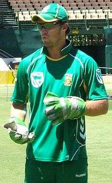 A man wearing a green top and cap, light green gloves and black goggles