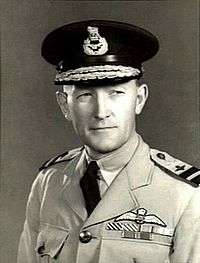 Head-and-shoulders portrait of man in light-coloured military uniform with ribbons and pilot's wings on chest, wearing dark peaked cap