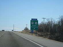 A green sign reads "ALT US 75, SH 16, Beggs, Muskogee" with an arrow. A blue plaque above it reads "CAMPING".