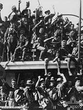 Cheering soldiers sitting and standing aboard the deck of a departing ship