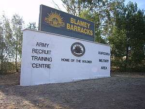 A sign stands surrounded by bushland. It features the Army's Rising Sun badge and reads: Blamey Barracks / Army Recruit Training Centre / Kapooka Military Area / Home of the Soldier.