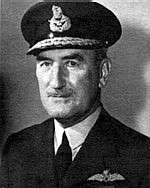 Head-and-shoulders portrait of man in dark  uniform with peaked cap and pilot's wings on left-breast pocket
