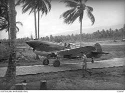 A single-engined propeller-driven monoplane moves down a narrow path between coconut palms.