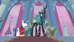 A white male unicorn in a red vest stares vacantly at a horse-like and dark-colored female monster with holes in her legs. They are on the steps of a stage, in a wedding setting.
