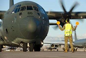Marshal in fluorescent jacket directing military transport aircraft on airfield