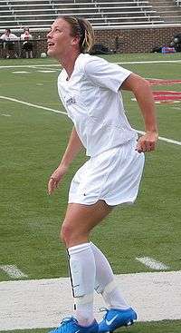 Wambach wearing a white uniform by a football field.