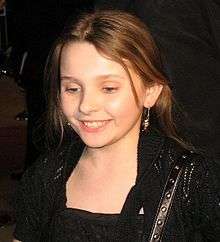 A young girl wearing a black dress looks down to her right while smiling.