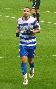 A footballer wearing a white football strip with blue hoops on the shirt.