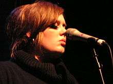 A woman wearing a black turtle neck with a microphone in front of her face
