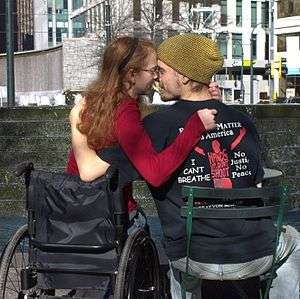 A woman in a wheelchair embraces a man in a chair