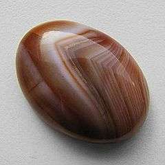 An oval cabochon of Lake Superior agate which displays the typical tight fortification banding in shades of reds, yellows and white.