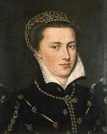A serene brown-haired woman, probably in her twenties, with a round face and clear skin and eyes, wears a richly embroidered and jeweled gown, wearing a jeweled headpiece. She wears gems in her ear lobes, and has a gem necklace. Her face is framed by a white collar with intricate embroidery work on its edging. Her demeanor is composed, and she has a slight smile.